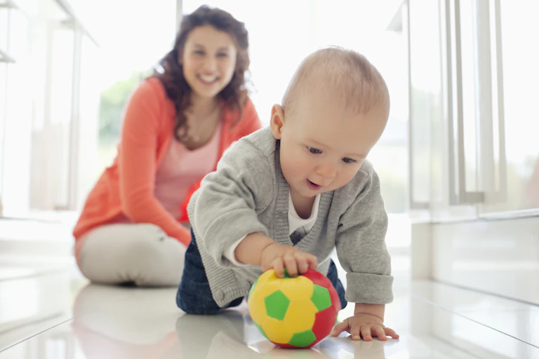 Mother watching baby playing with ball