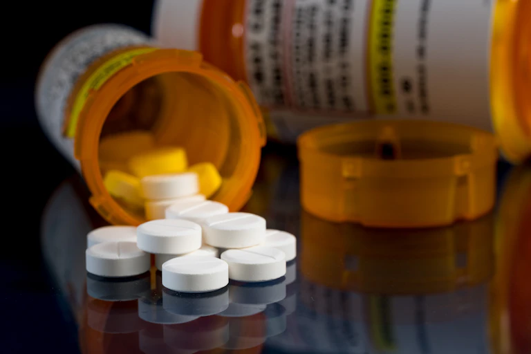Opioid tablets spilling out of the prescription bottle onto the table.