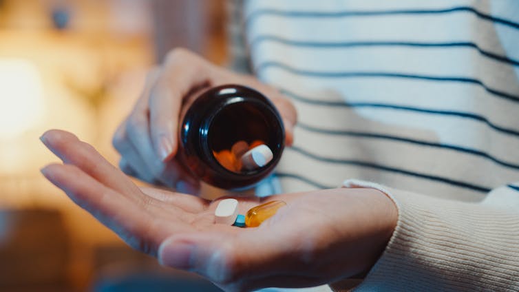 A woman holding a bottle of pills in one hand and examining the contents in the palm of another hand.