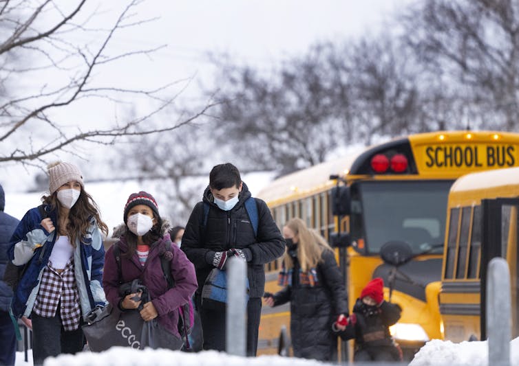 Students exit a school bus wearing masks in the snow
