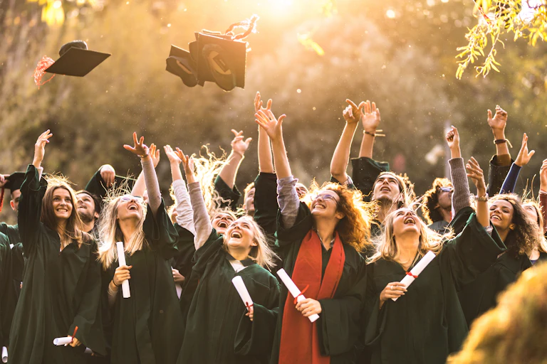 a number of graduates in robes throw mortarboards in air