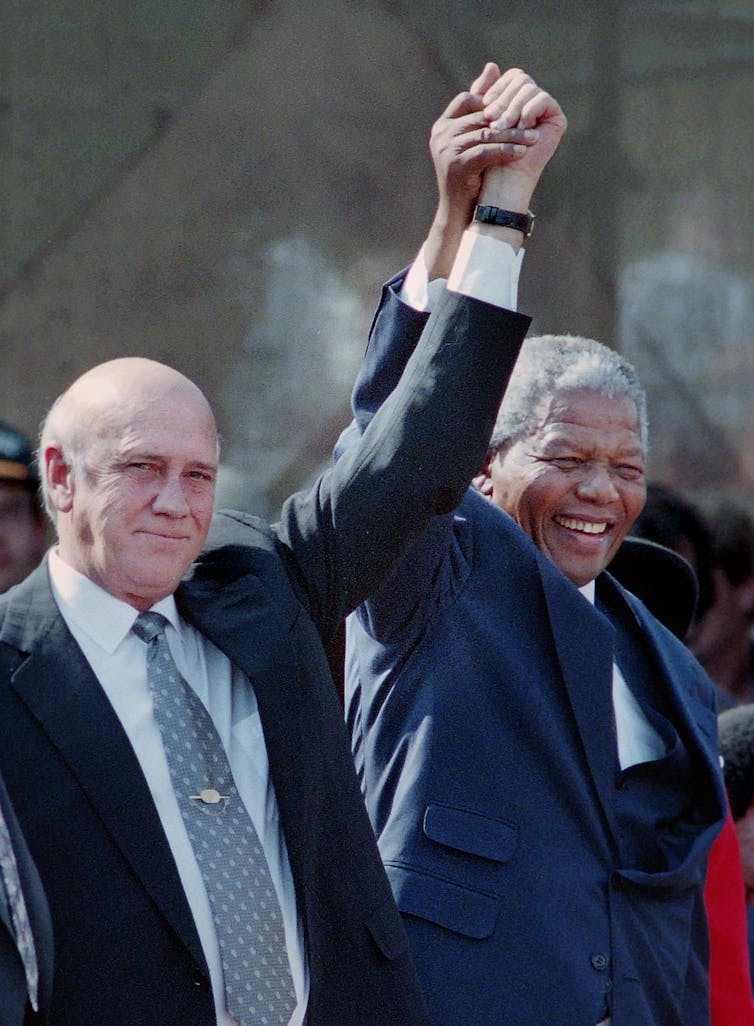 A Black man and a white man raise their arms together and hold hands.