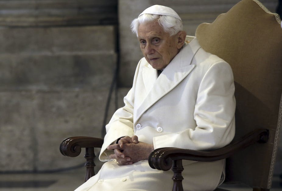 Pope Benedict sits on a yellow chair, wearing a white coat and skullcap.