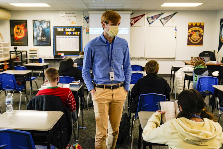 A man stands in a classroom, with several children seated at desks