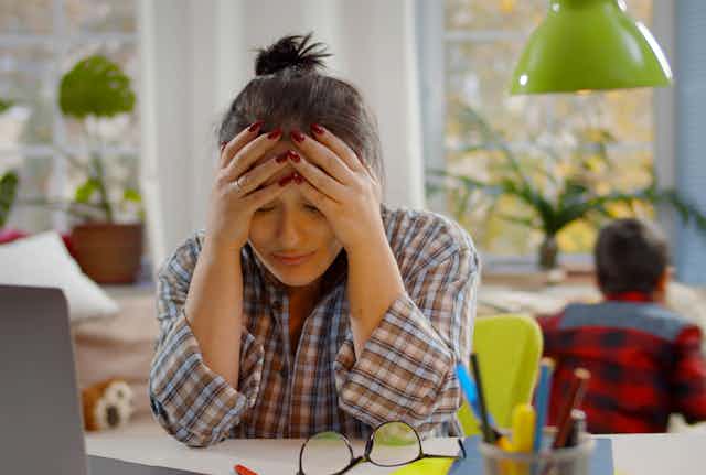 Woman with head in hands struggling to study as children play in the background