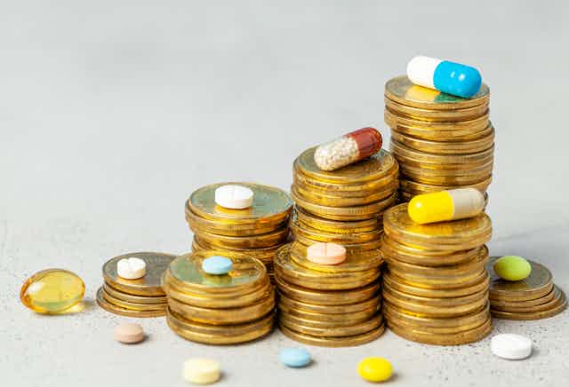 Stacks of coins with different coloured capsules and pills scattered around them.