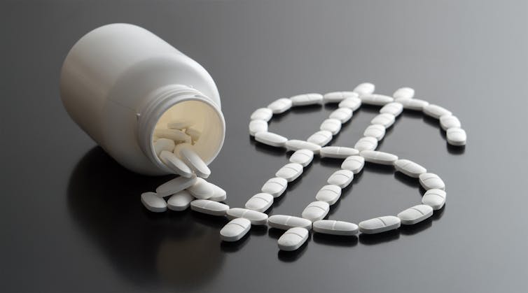 A medicine bottle tipped on its side, with white caplets arranged in the shape of a dollar sign