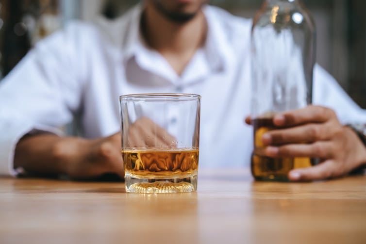 A man drinking whiskey, with a glass and bottle in front of him