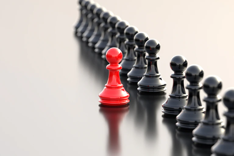 A row of black chess pawns with one red pawn stepped out of line, as if leading.