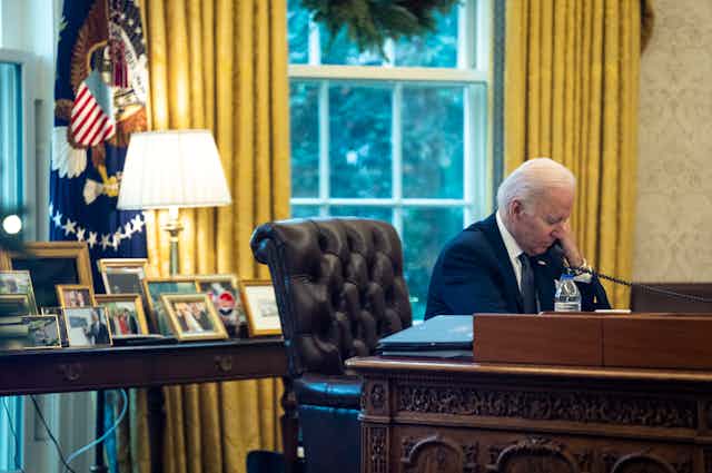 Joe Biden making phone call from his desk in the Oval Office.