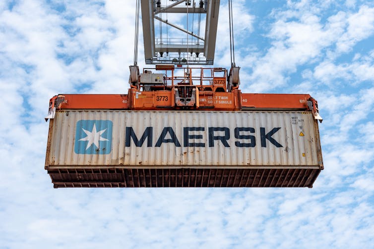 A Maersk shipping container hoisted in the air by a crane.