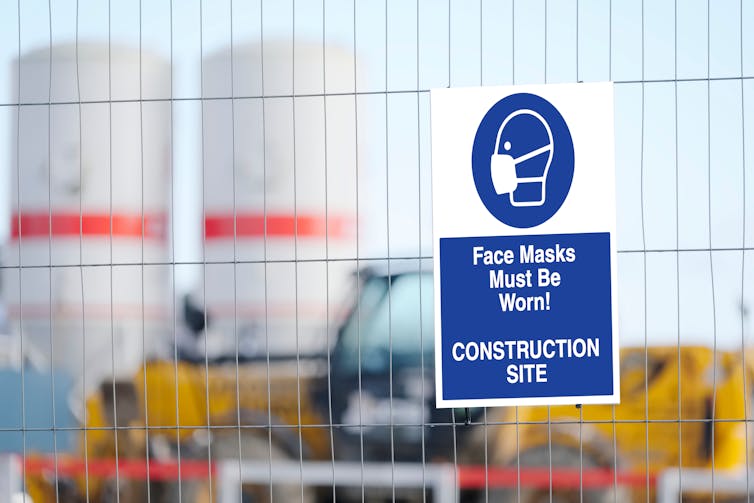 Building site fence, with sign saying face masks must be worn.