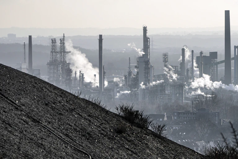 A coal mine dump in the foreground with an oil refinery behind it.