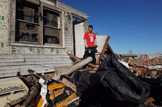 A man stands on the the shattered front porch of what remains of a house struck by a tornado.