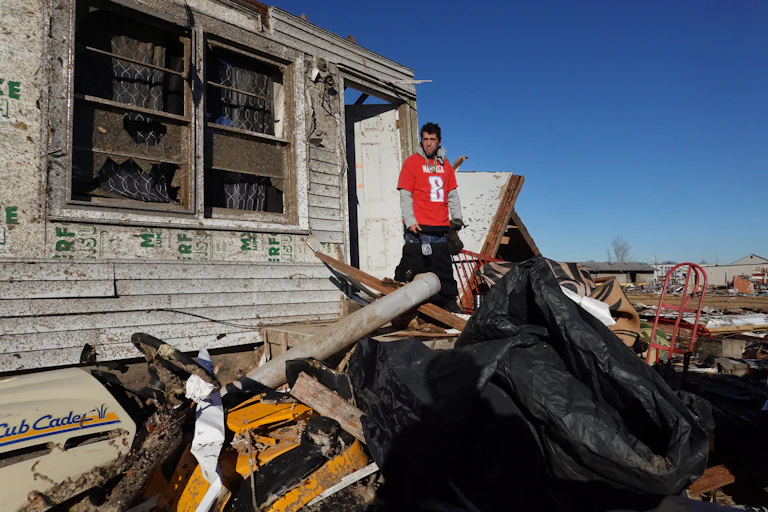 A man stands on the the shattered front porch of what remains of a house struck by a tornado.