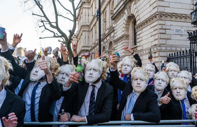 Protestors wearing Boris Johnson masks holding up beers outside Downing Street. 