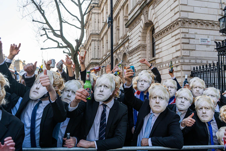 Protestors wearing Boris Johnson masks holding up beers outside Downing Street.