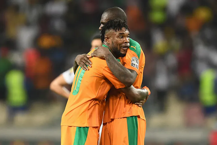 Two football players, tired and sweaty and wearing orange, hug one another.