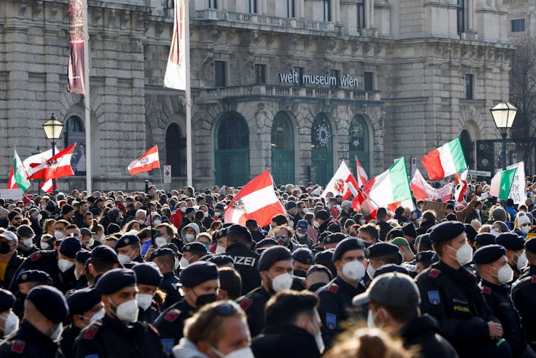 Line of police wearing masks next to crowd of protestors carrying flags.