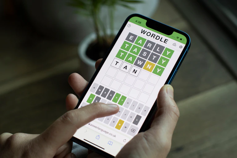 A person's hands hold a phone with the green, grey and yellow squares of the Wordle grid on the screen.