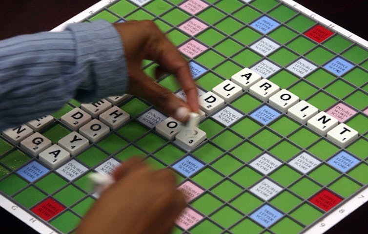A Scrabble player places tiles to spell a word on a green Scrabble board.