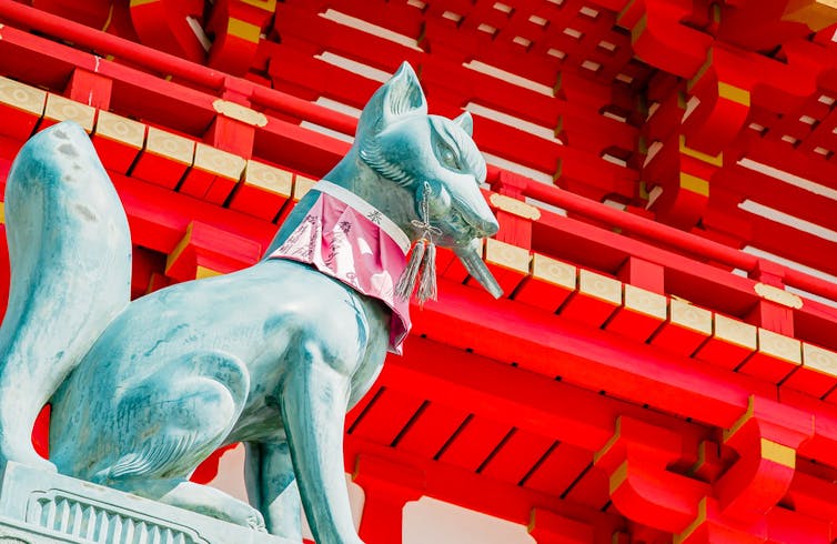 Fox statue standing against background of Shinto shrine