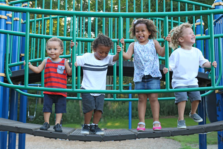 Four children stand on a playground bridge structure.