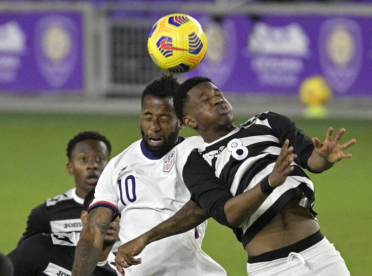 Two soccer players colliding while trying to head a ball