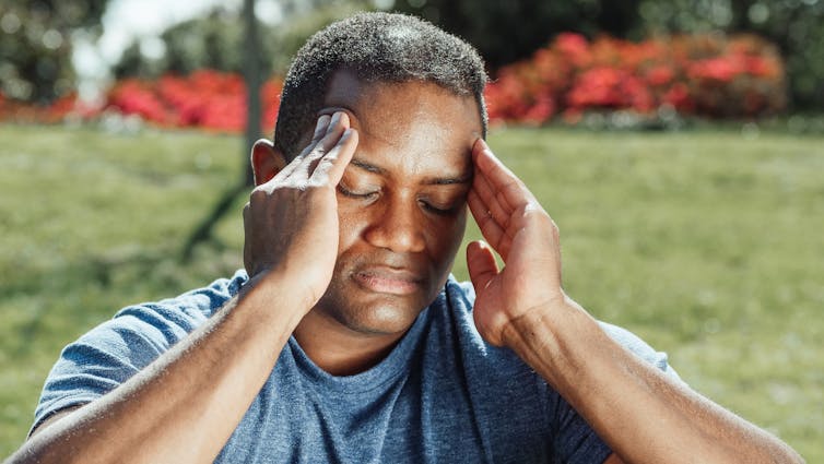 Man sitting on grass with his eyes closed and his fingertips on his temples
