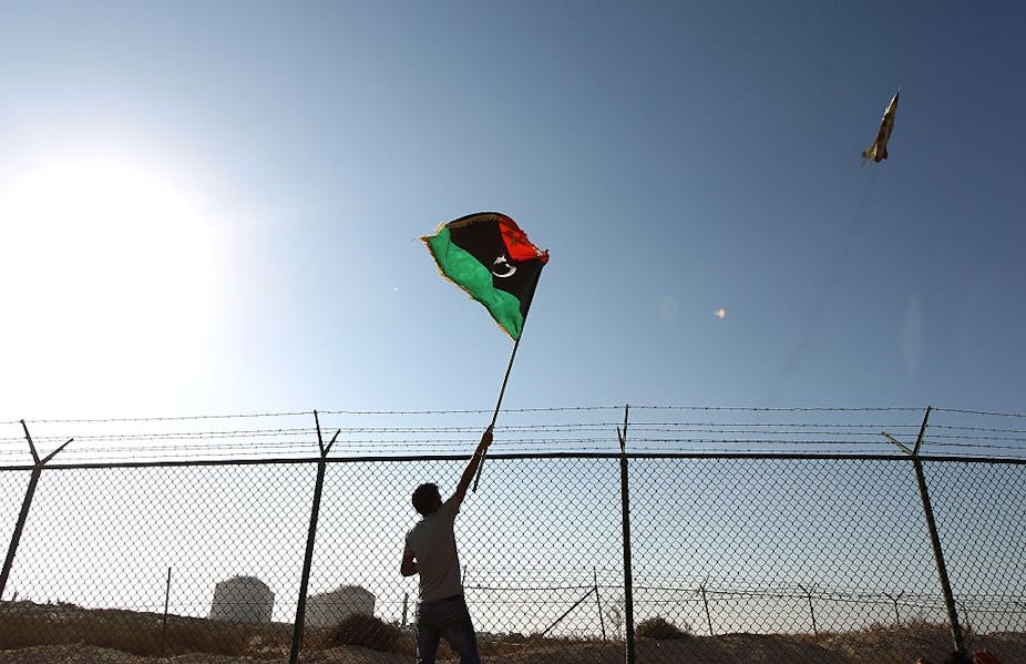  A man waves a Libyan flag as a fighter jet flies by Zueitina oil terminal in 2016.  Abdullah Doma/AFP via Getty Images  A man waves a Libyan flag