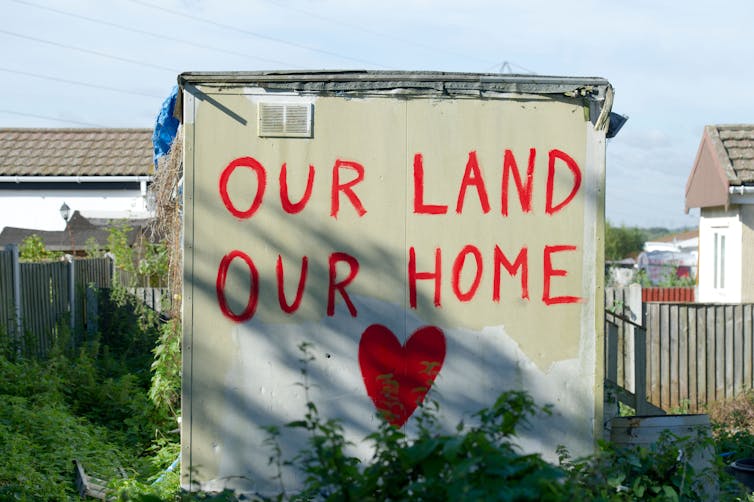 The side of an outhouse painted with the message 'Our land, our home' and a red heart.