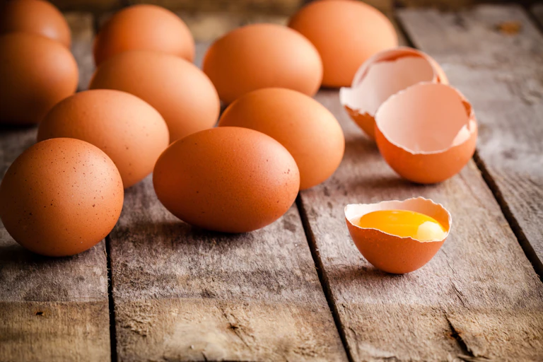 Huevos sobre una mesa de madera. Uno de ellos ya cascado.