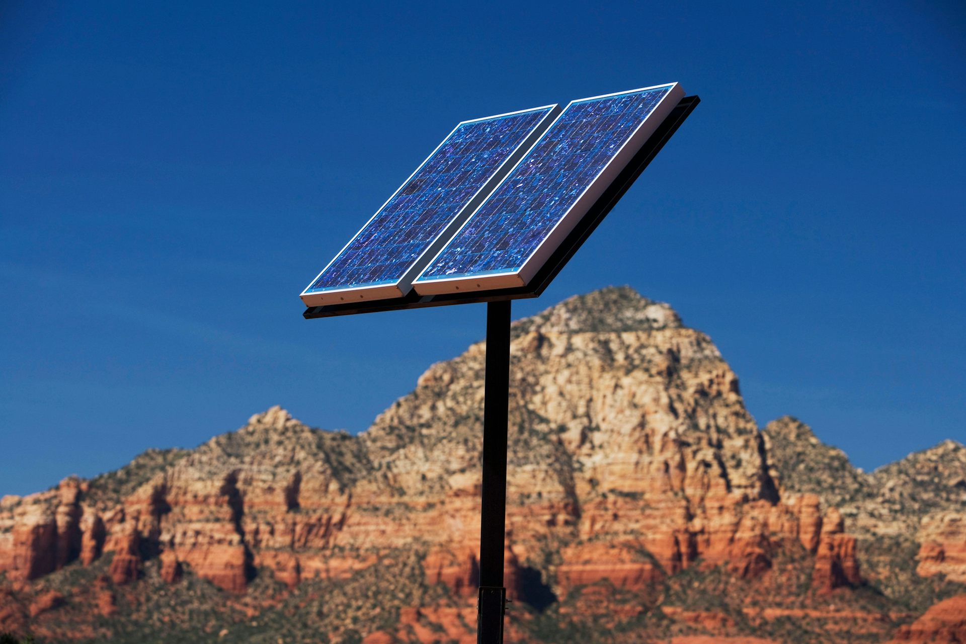 A solar panel on the end of a pole in a desert.