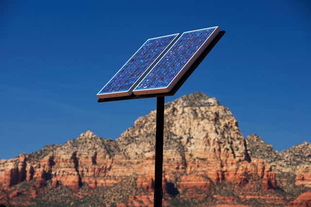 A solar panel on the end of a pole in a desert.