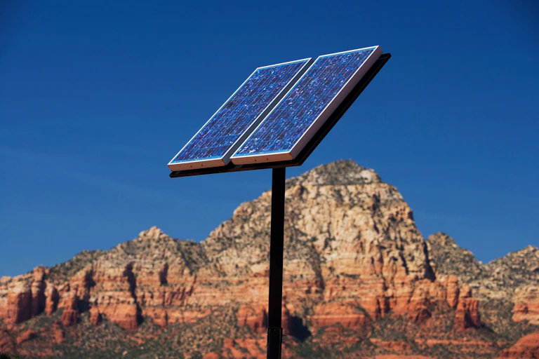 A solar panel on the end of a pole in a desert.