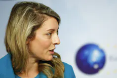 A woman with blonde hair wearing a green jacket is seen in profile.
