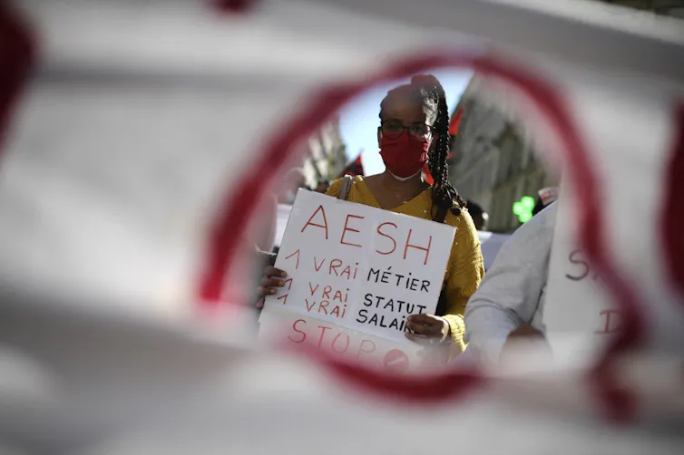 Une jeune femme brandit une pancarte « AESH, un vrai métier, un vrai statut, un vrai salaire » lors des manifestations d’octobre 2021