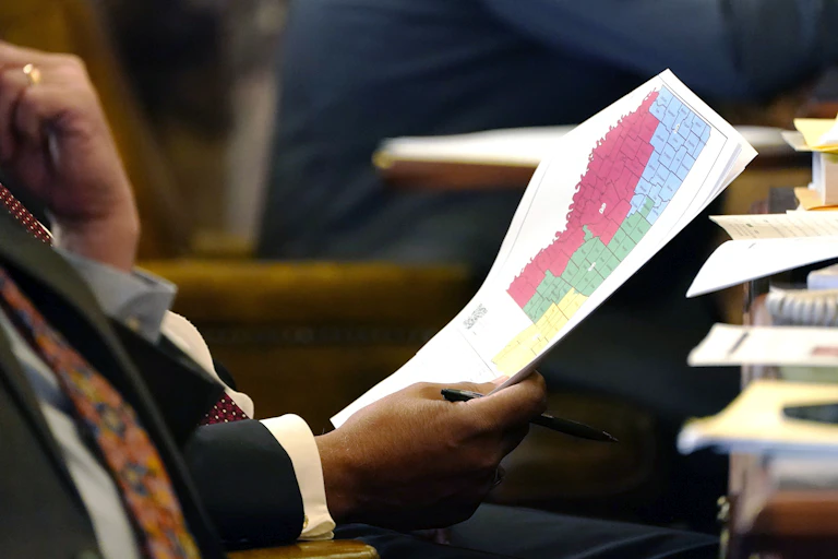 A man holding a map divided into colored blocks, while sitting at a desk.