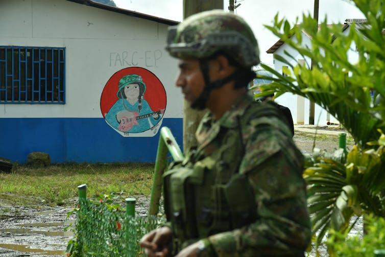 A soldier clad in military wear stands in front of a painted mural that says 