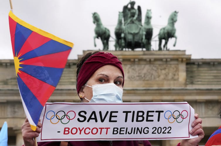 A woman wearing a medical face mask holding a sign that says 'Save Tibet: Boycott Beijing 2022.'