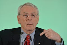 A man wearing glasses sitting in front of a teal background