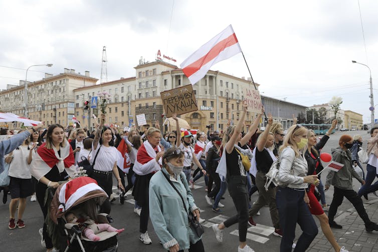 women including some pushing baby strollers carry signs and march in a protest