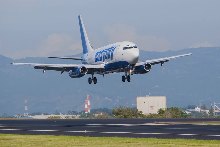 a jetliner with its landing gear down just above a runway with mountains in the background