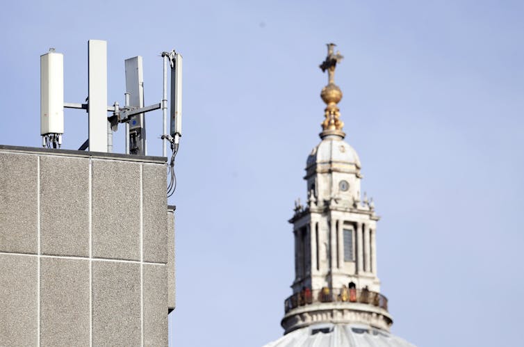 Four vertical rectangular devices mounted on the corner of a roof of a building with a church spire in the background
