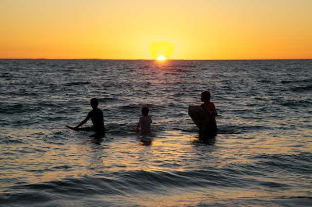 Three kids in the ocean at sunset