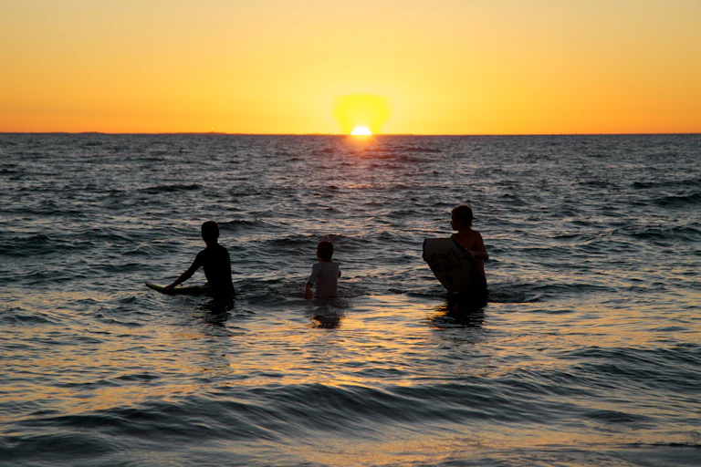Three kids in the ocean at sunset