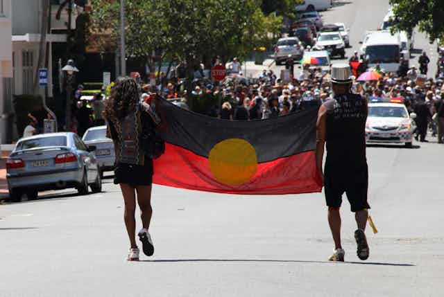 Two protestors march with the Aboriginal Flag