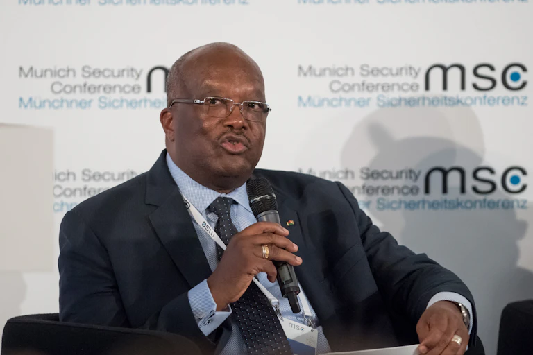 A man wearing a suit is seated while holding a microphone at a seminar