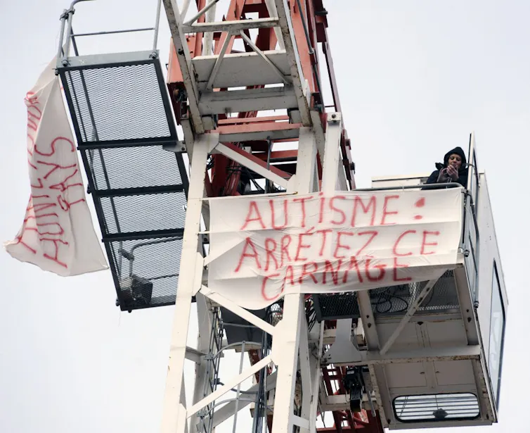 Panneau installé en haut d’une grue par Estelle Ast, mère d’un enfant autiste de huit ans, indiquant : « Autisme : Stop the carnage »