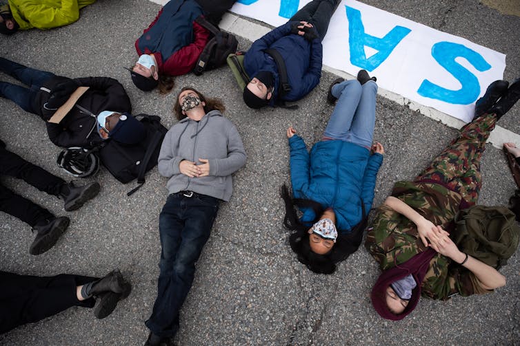 Protestors in COVID-19 face masks are lying on the road in a protest.